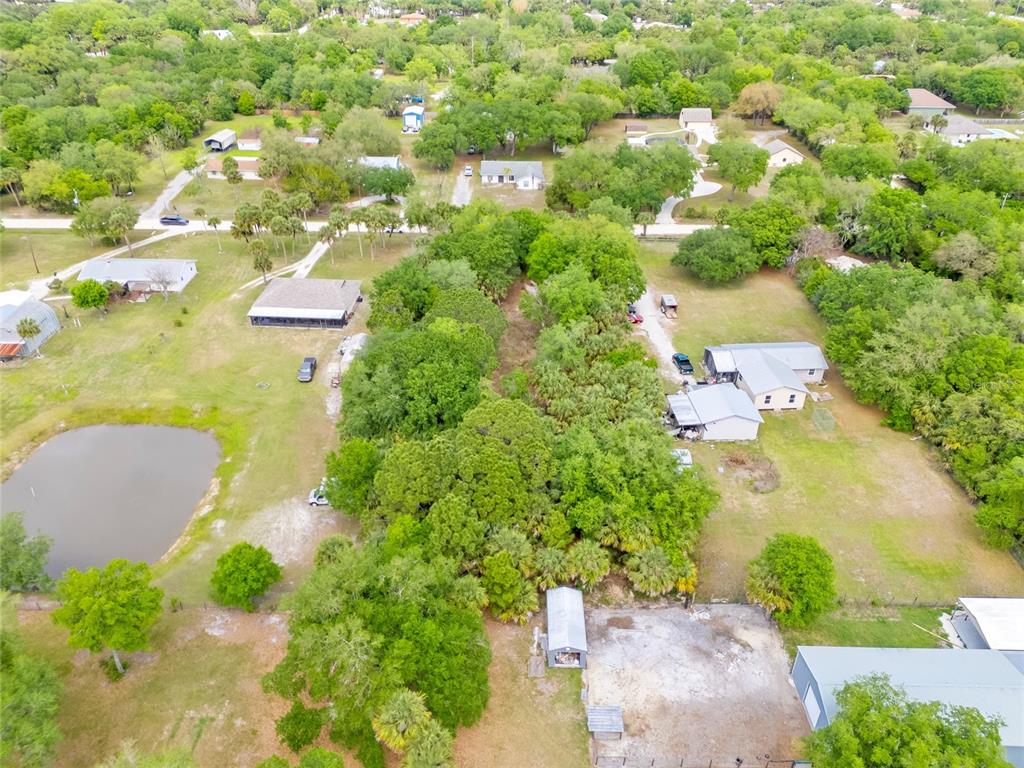 An aerial view shows several houses, outbuildings, and a small pond on a wooded lot — 5175 VACARO AVENUE, COCOA, FL