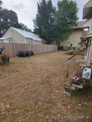 A backyard features a wooden fence, a small white house, and several black trash bags — 47 N 5TH STREET, MACCLENNY, FL