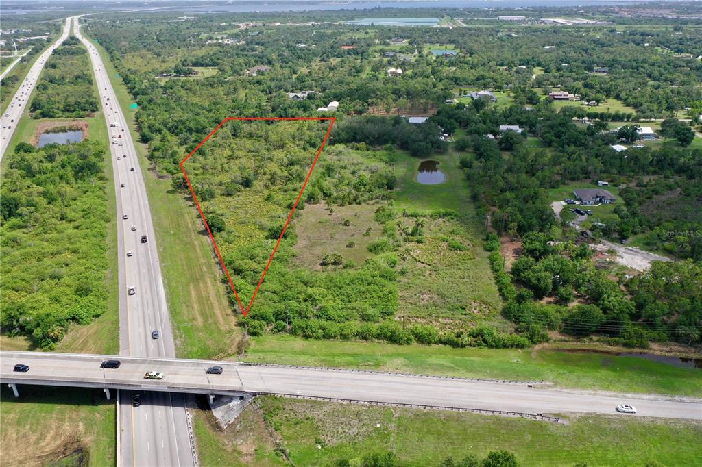 An aerial view shows a triangular plot of land outlined in red next to a highway — 24646 TANGELO AVENUE, PORT CHARLOTTE, FL