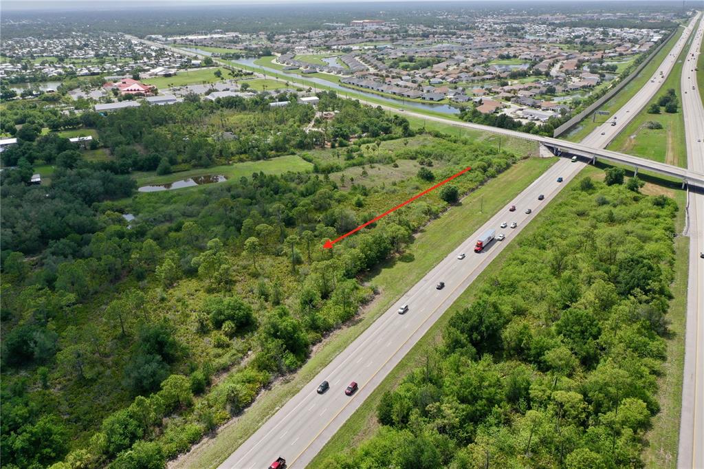 An aerial view shows a wooded lot adjacent to a highway with an overpass nearby — 24646 TANGELO AVENUE, PORT CHARLOTTE, FL