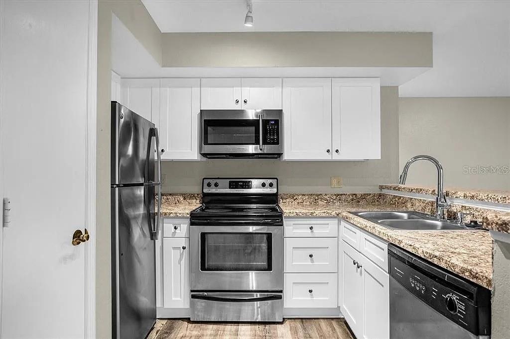 A kitchen features white cabinets, stainless steel appliances, and granite countertops — 7210 WESTPOINTE BOULEVARD UNIT 1323, ORLANDO, FL