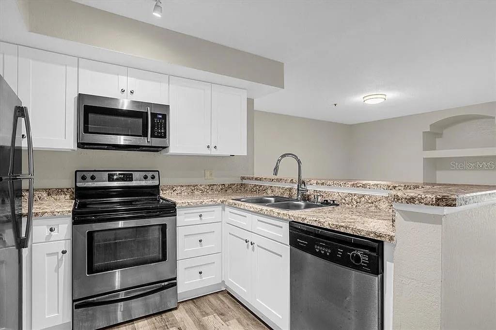 A kitchen features white cabinets, stainless steel appliances, and granite countertops — 7210 WESTPOINTE BOULEVARD UNIT 1323, ORLANDO, FL