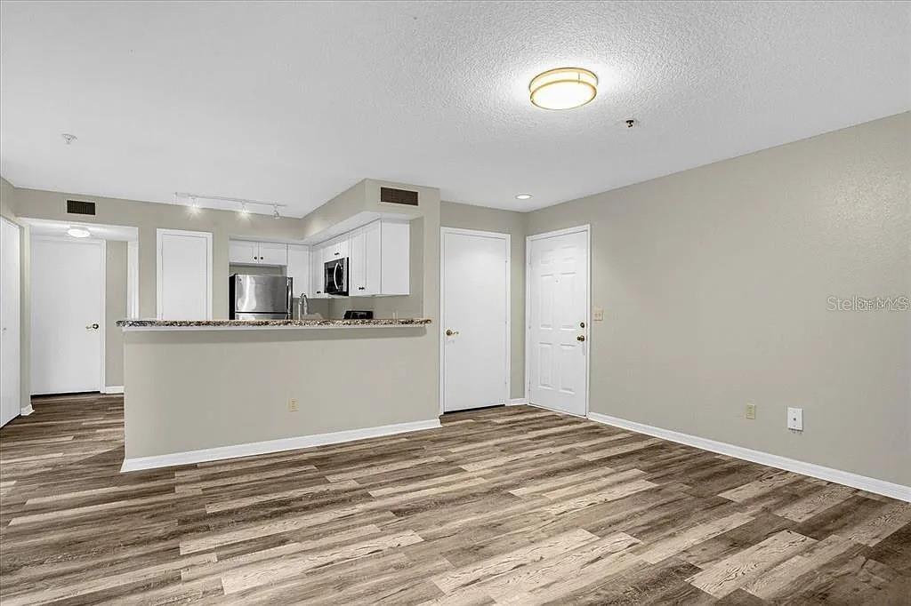 An open-concept living area features wood-look flooring and a kitchen with white cabinetry — 7210 WESTPOINTE BOULEVARD UNIT 1323, ORLANDO, FL