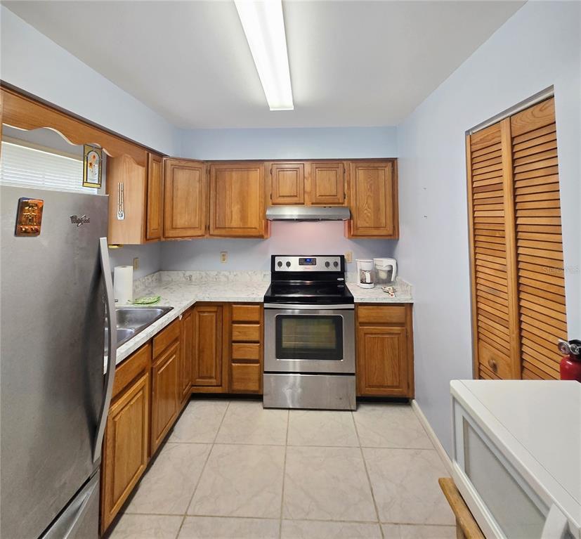 A kitchen with wooden cabinets, stainless steel appliances, and light-colored tile flooring — 41 N 20TH ST UNIT 18, HAINES CITY, FL