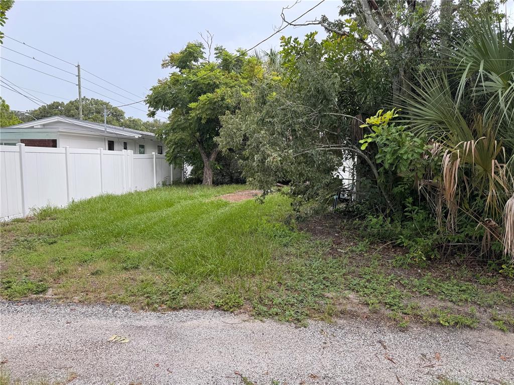 A grassy, partially wooded vacant lot sits next to a white vinyl fence and house — 766 51ST AVENUE N, ST PETERSBURG, FL