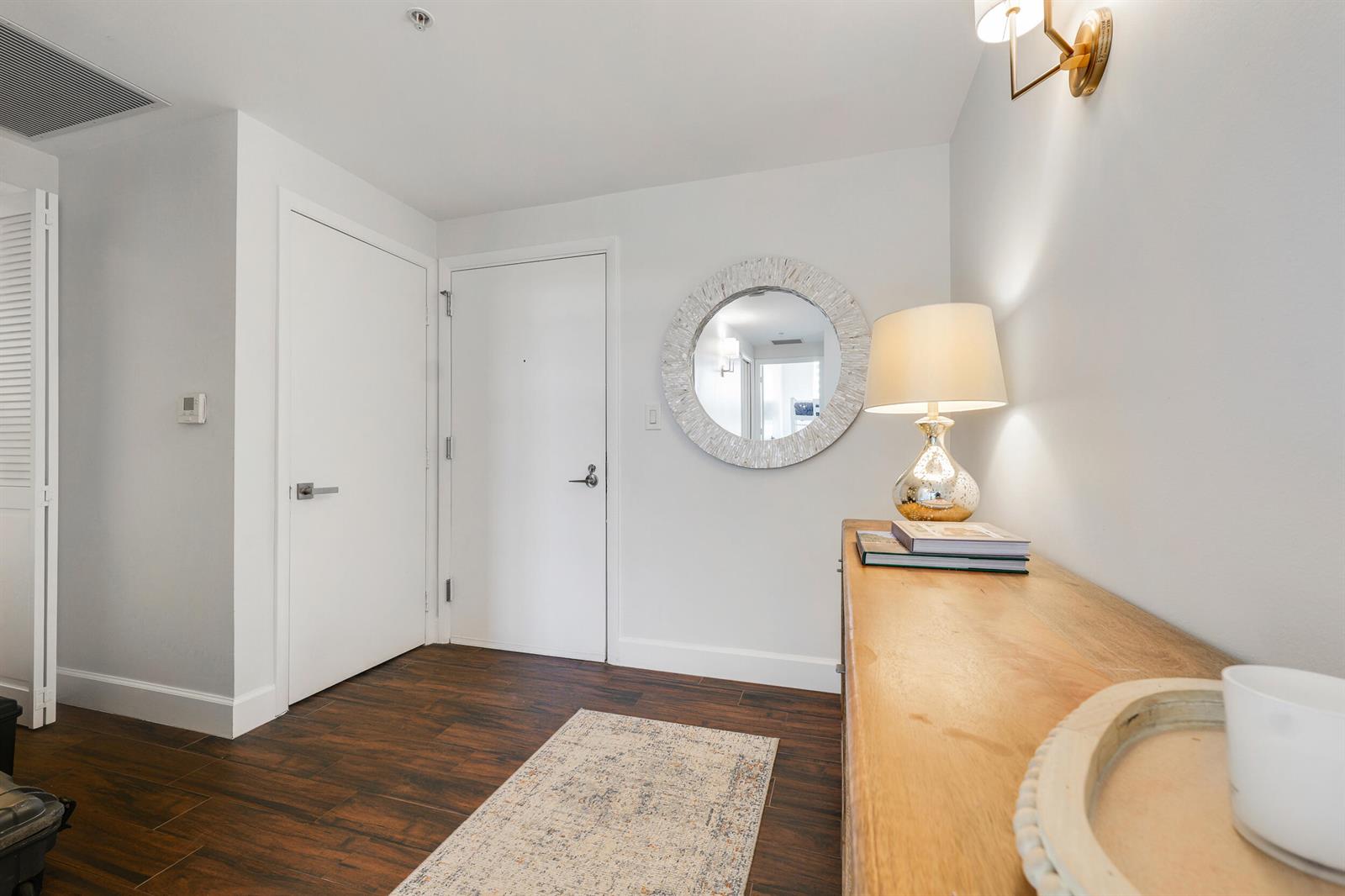 A hallway features dark wood floors, white walls, a round mirror, and a wooden console table — 550 Okeechobee Boulevard # 622, West Palm Beach FL 33401, WEST PALM BEACH, FL