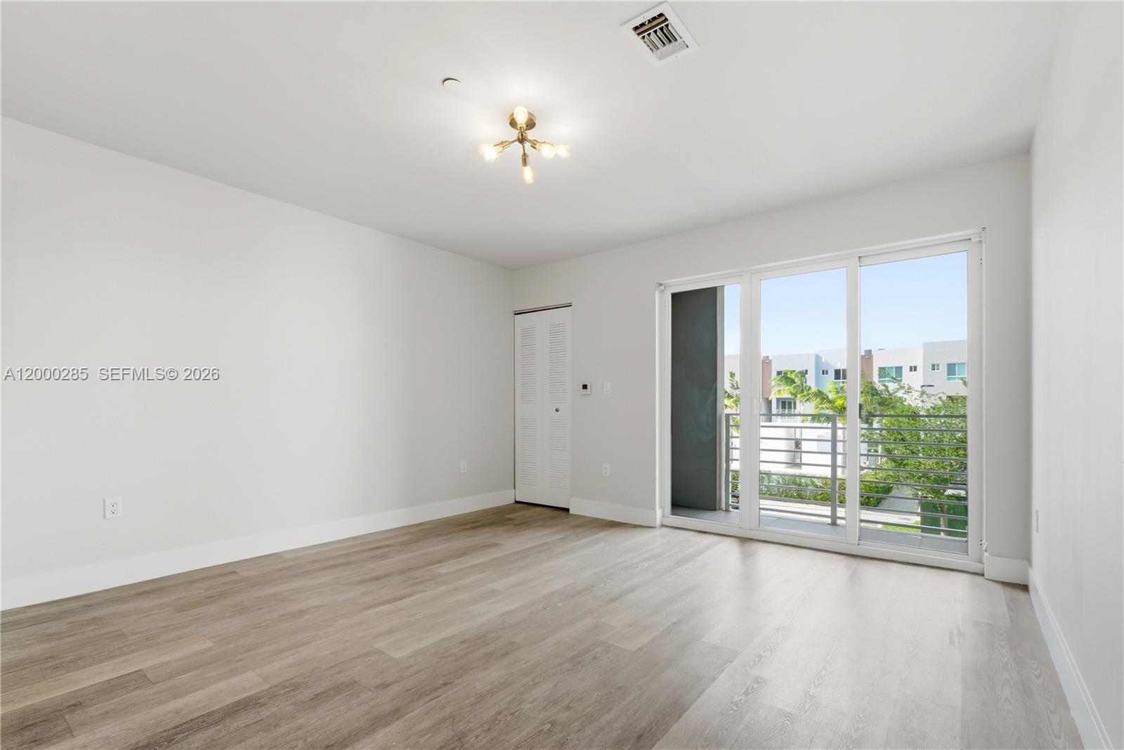 A bright bedroom features light wood-look flooring, a modern light fixture, and a sliding glass door — 2505 NE 193rd St # 4215, Miami FL 33180, MIAMI, FL