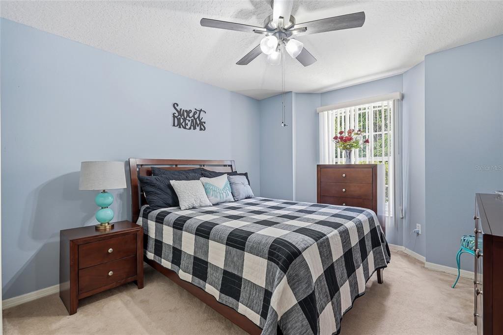 A bedroom features light blue walls, a plaid bedspread, a ceiling fan, and wooden furniture — 12512 HOLLYBROOK LANE, HUDSON, FL