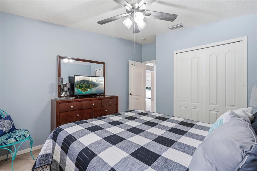 A bedroom features a plaid bedspread, a wooden dresser with a mirror, and a ceiling fan — 12512 HOLLYBROOK LANE, HUDSON, FL