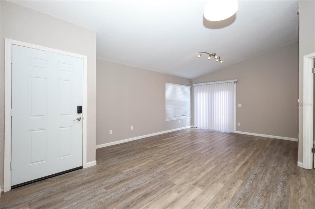 An empty living room features light-colored walls, wood-look flooring, a white front door, and sliding doors — 5443 BLUEBERRY DRIVE, ORLANDO, FL