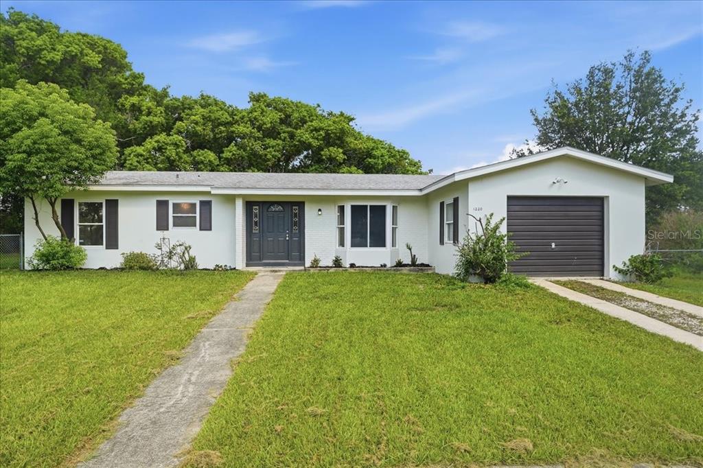 A single-story white house with a dark front door, a garage, and a front lawn — 1220 SIENNA COURT, DELTONA, FL