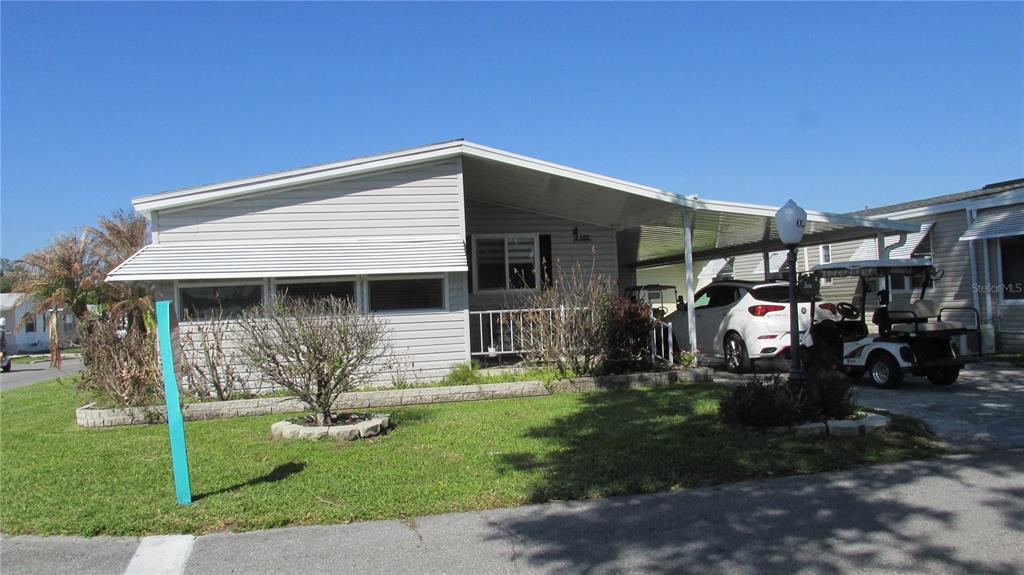 A single-story manufactured home with light gray siding, a carport, and a golf cart parked — 102 NEWCASTLE BOULEVARD, HAINES CITY, FL