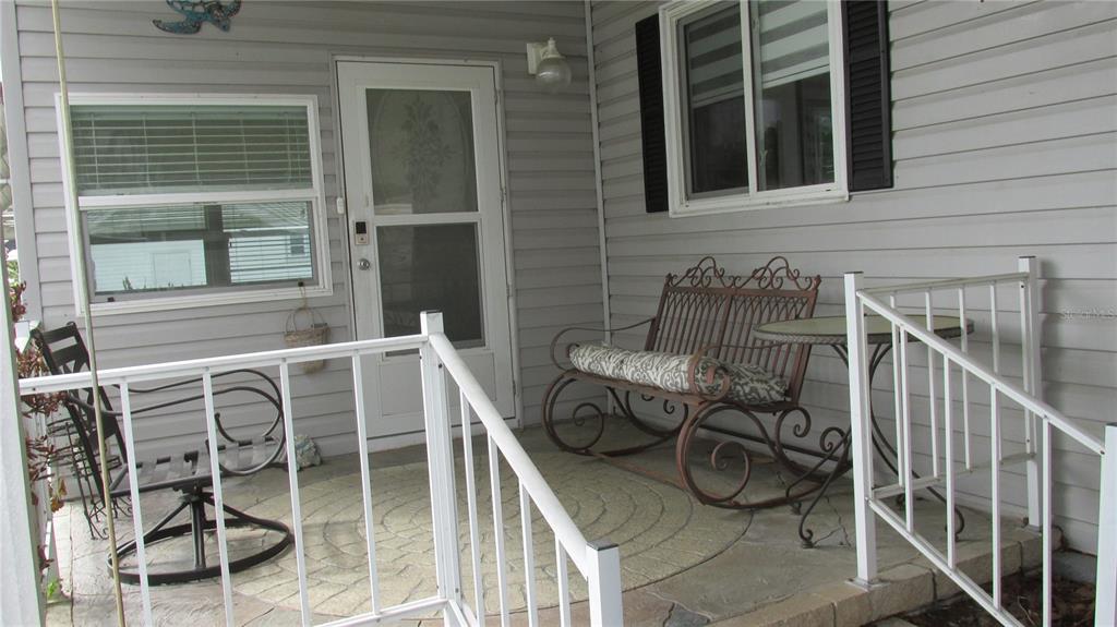 A covered porch features light gray siding, a white storm door, and outdoor seating furniture — 102 NEWCASTLE BOULEVARD, HAINES CITY, FL