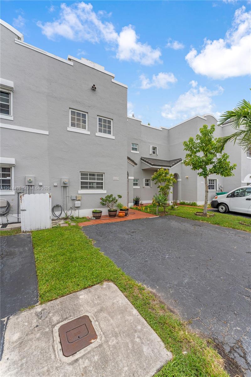 The exterior of a gray two-story townhouse features a small front yard and driveway — 12427 NW 7th Ln, Miami FL 33182, MIAMI, FL
