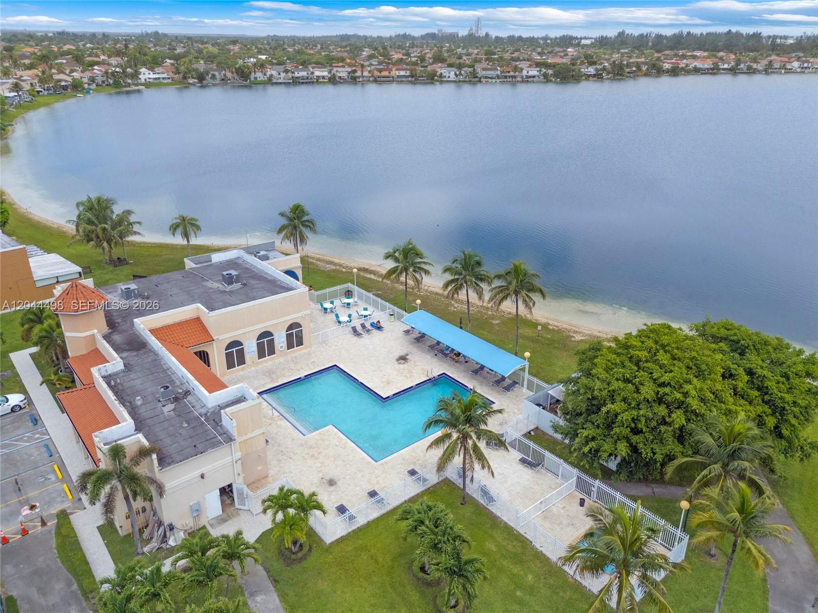 An aerial view shows a community clubhouse with an L-shaped pool beside a lake — 12427 NW 7th Ln, Miami FL 33182, MIAMI, FL