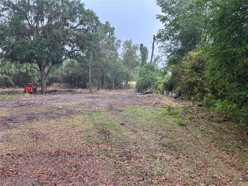 A cleared, dirt-covered lot features a small red tractor and dense surrounding trees — 4724 SW 63RD BOULEVARD, GAINESVILLE, FL