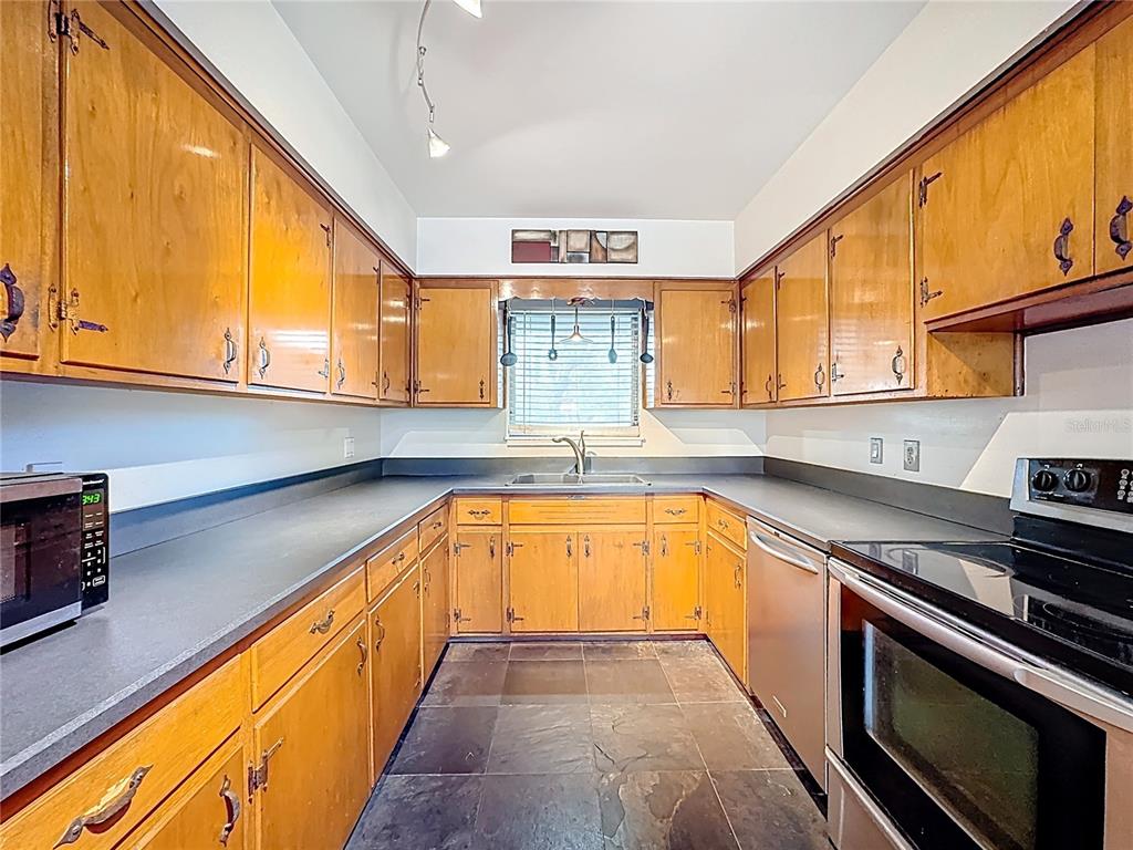 A galley kitchen features wood cabinets, dark countertops, and slate tile flooring — 512 N LAKEMONT AVENUE, WINTER PARK, FL