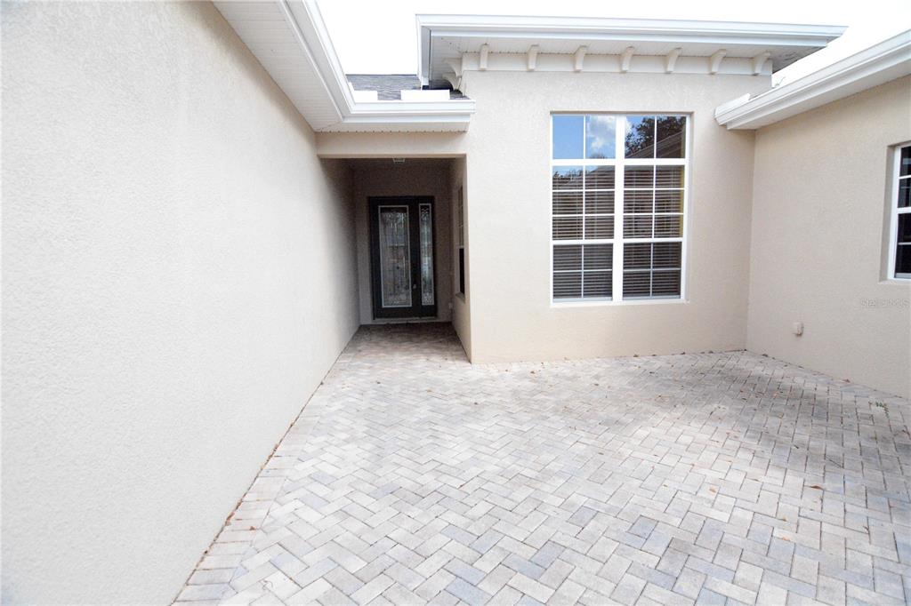 A paved courtyard leads to the front entrance of a house with beige stucco walls — 2294 SIFIELD GREENS WAY UNIT 2294, SUN CITY CENTER, FL