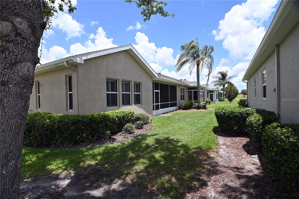 The exterior of two tan houses with screened lanais and landscaped yards under a blue sky — 2294 SIFIELD GREENS WAY UNIT 2294, SUN CITY CENTER, FL