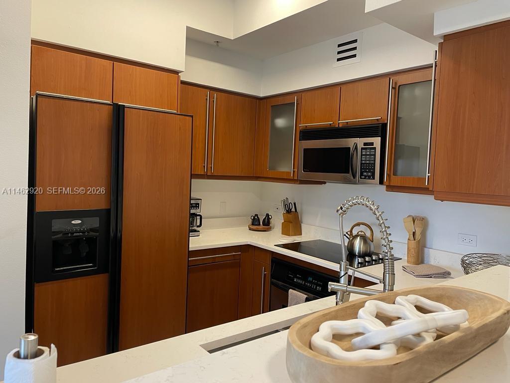 A kitchen features wood cabinets, white countertops, stainless steel appliances, and a decorative wooden bowl — 2069 S Ocean Dr, Hallandale Beach FL 33009, HALLANDALE BEACH, FL