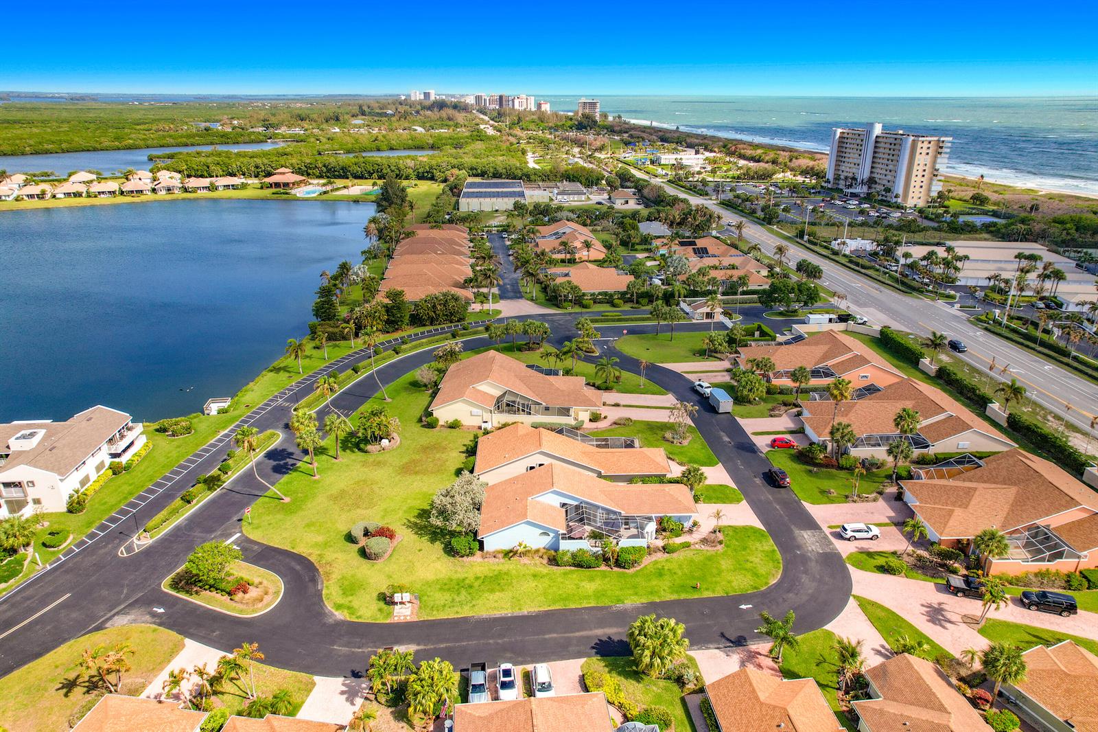 An aerial view shows a residential neighborhood with houses, a lake, and a nearby beach — 208 River Walk, Fort Pierce FL 34949, FORT PIERCE, FL
