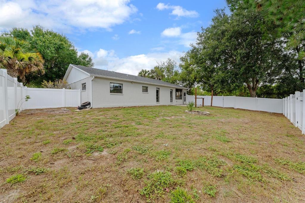 A backyard with a light-colored house, white vinyl fencing, and sparse grass — 7505 BRAMBLEWOOD DRIVE, PORT RICHEY, FL