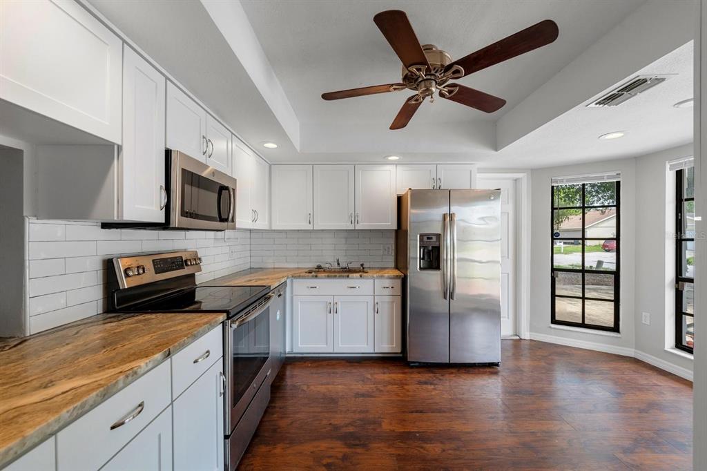 A kitchen with white cabinets, stainless steel appliances, wood-look flooring, and a ceiling fan — 7505 BRAMBLEWOOD DRIVE, PORT RICHEY, FL