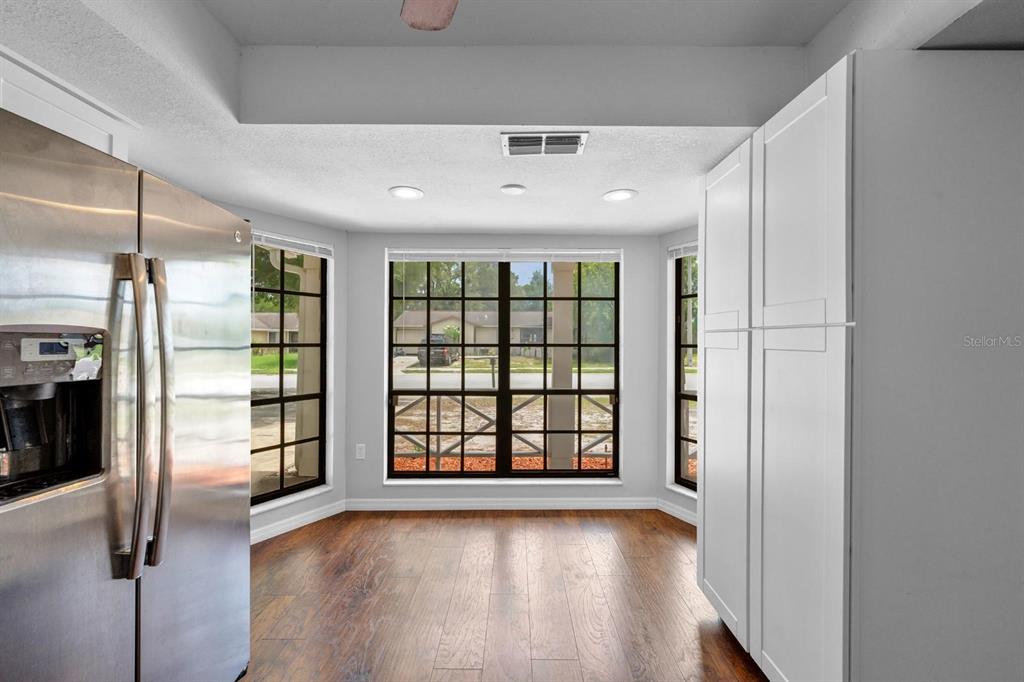A kitchen breakfast nook features large windows, white cabinetry, and wood-look flooring — 7505 BRAMBLEWOOD DRIVE, PORT RICHEY, FL