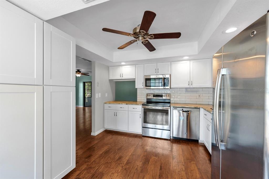 A kitchen with white cabinets, stainless steel appliances, granite countertops, and wood-look flooring — 7505 BRAMBLEWOOD DRIVE, PORT RICHEY, FL