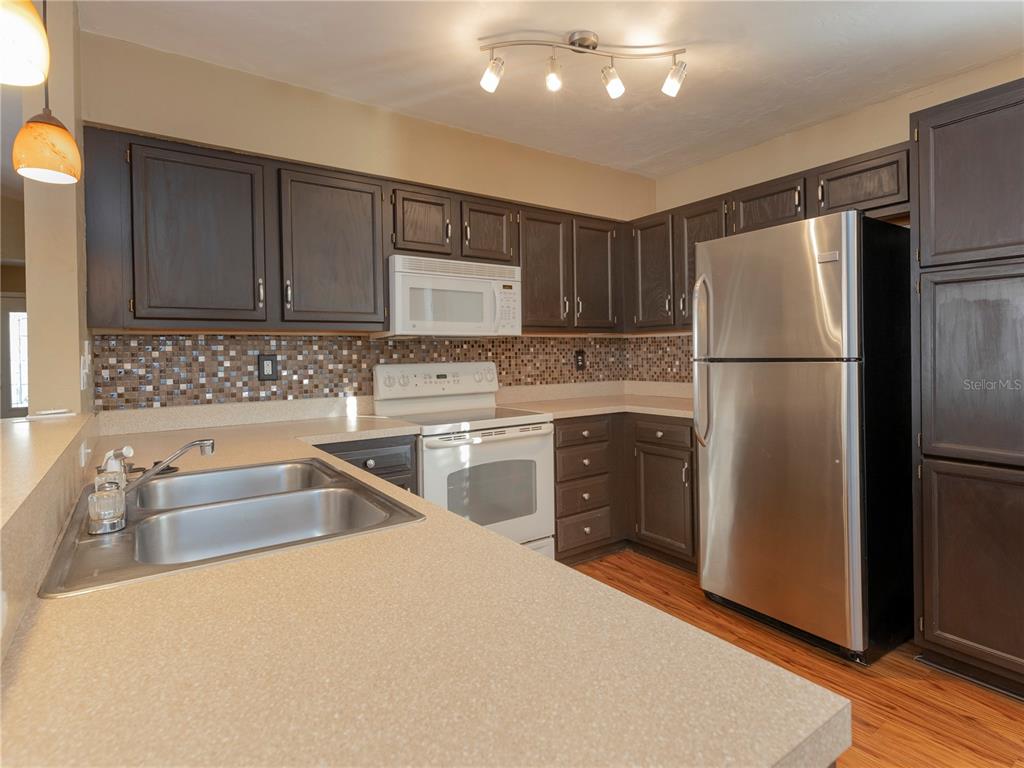 A kitchen features dark wood cabinets, stainless steel appliances, a tiled backsplash, and laminate countertops — 3776 NW 26TH TERRACE, GAINESVILLE, FL