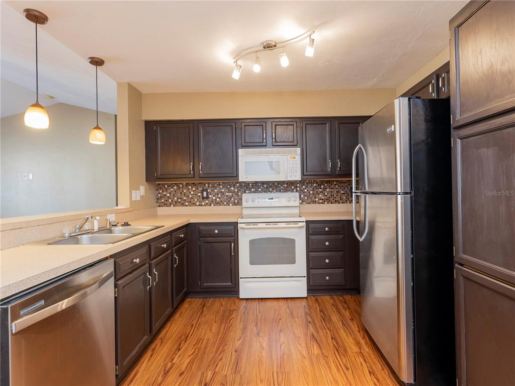 A kitchen features dark wood cabinets, stainless steel appliances, a mosaic backsplash, and wood-look flooring — 3776 NW 26TH TERRACE, GAINESVILLE, FL