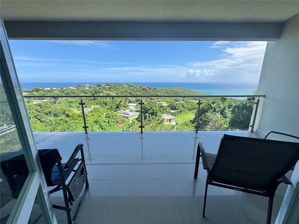 A balcony with tile flooring and a glass railing overlooks a lush landscape and ocean — El Cocal Country Club BO. CAMINO NUEVO UNIT 2, YABUCOA, PR