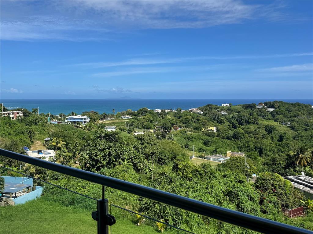 A balcony railing overlooks a lush, hilly landscape with houses and a distant ocean view — El Cocal Country Club BO. CAMINO NUEVO UNIT 2, YABUCOA, PR
