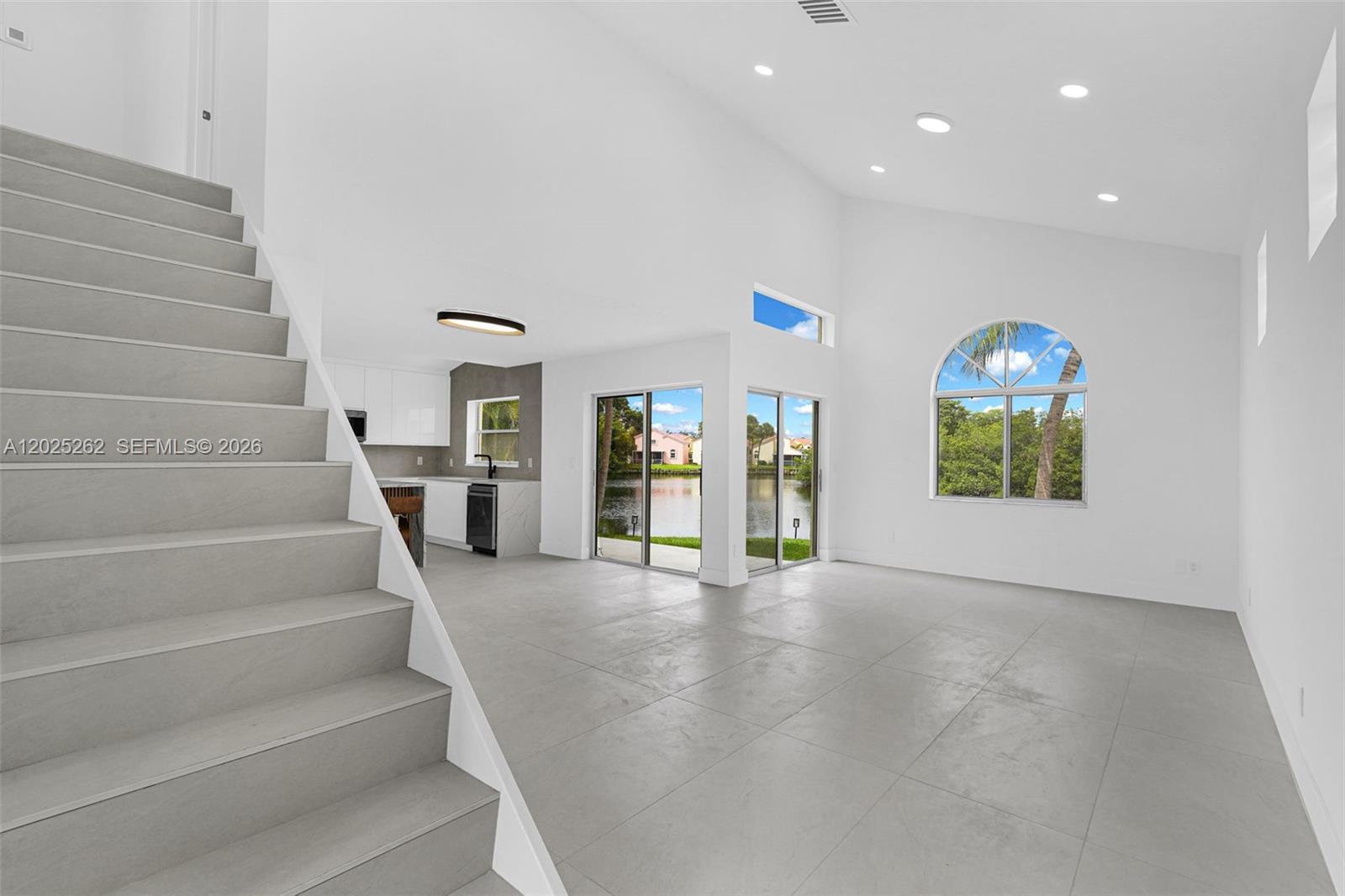A modern living room features a staircase, tile flooring, high ceilings, and a lake view — DANIA BEACH, FL