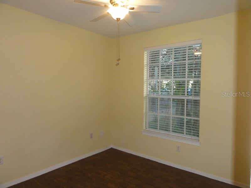 A bedroom with yellow walls, dark wood-look flooring, a ceiling fan, and a window — 830 GRAND REGENCY POINTE UNIT 103, ALTAMONTE SPRINGS, FL