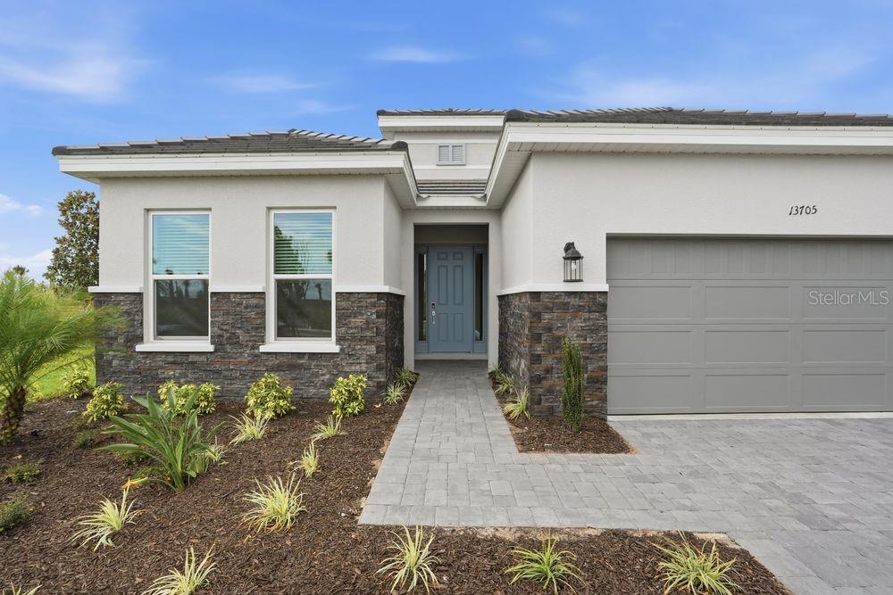 A single-story house exterior features a gray garage, stone veneer accents, and a paved walkway — 13705 IONA AVENUE, PALMETTO, FL