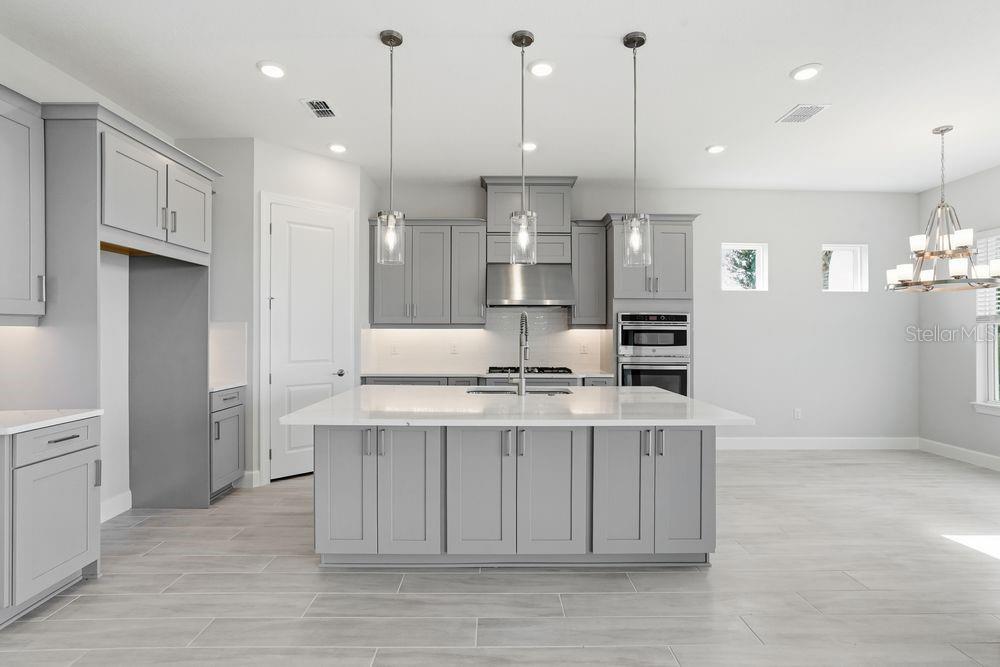 A modern kitchen features gray cabinets, a large white island, and stainless steel appliances — 13705 IONA AVENUE, PALMETTO, FL