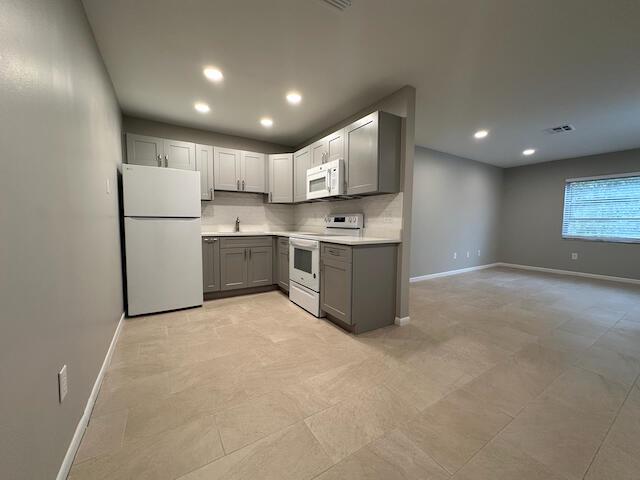 A kitchen with gray cabinets, white appliances, and light tile flooring opens to a living area — 1741 N 3rd Ave Avenue N # 6, FL 33460, FL