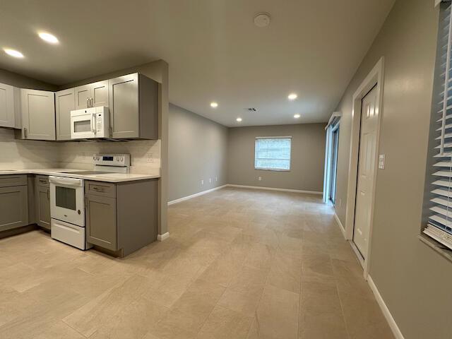 A kitchen with gray cabinets and white appliances opens into a spacious, tiled living area — 1741 N 3rd Ave Avenue N # 6, FL 33460, FL