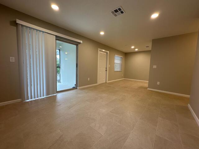 An empty living area features beige tile flooring, recessed lighting, and a sliding glass door — 1741 N 3rd Ave Avenue N # 6, FL 33460, FL