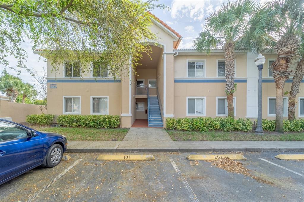 A two-story apartment building exterior features tan stucco walls, blue trim, and a concrete walkway — 13232 GALICIA STREET UNIT 101, ORLANDO, FL