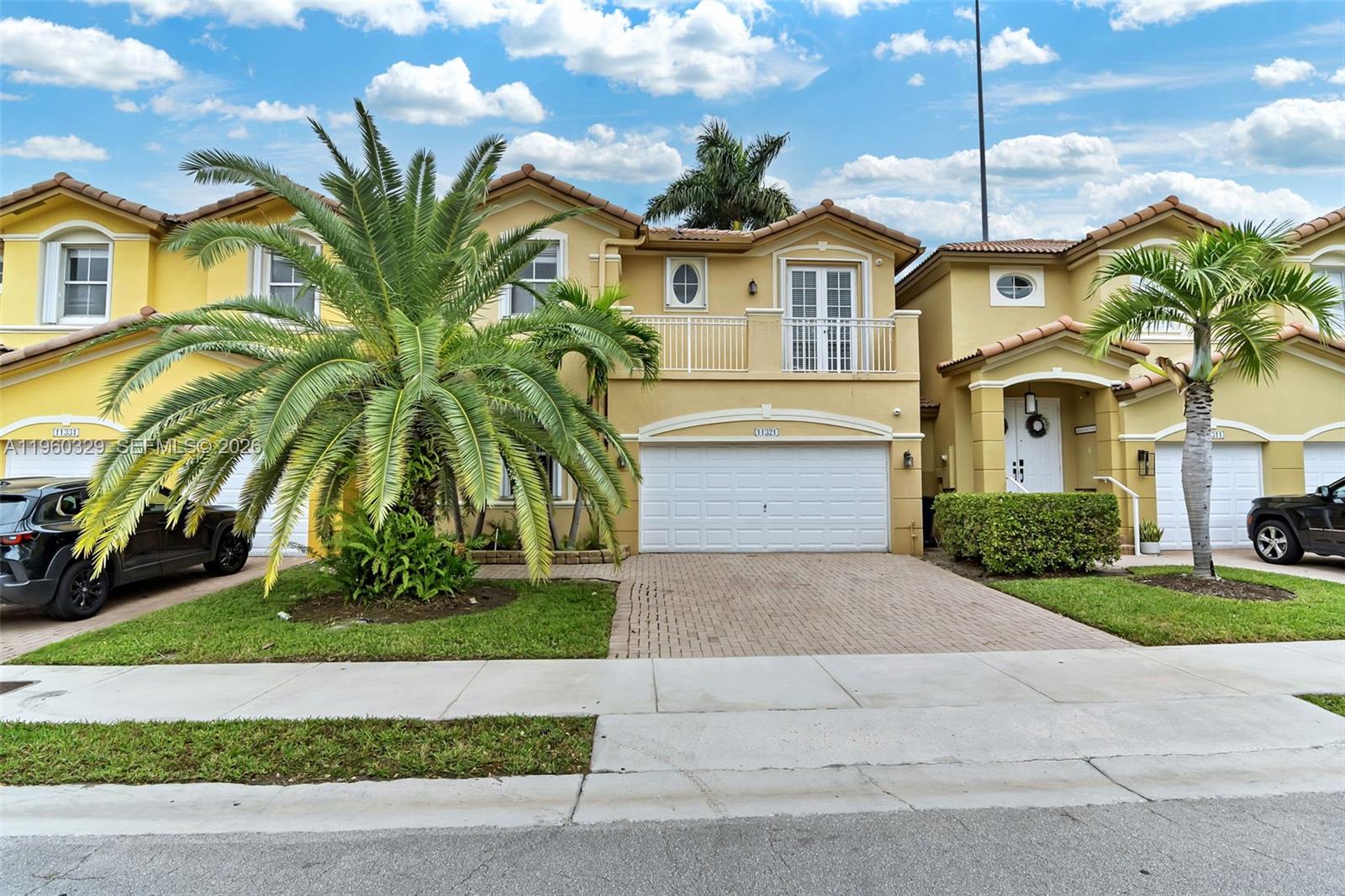 A two-story yellow stucco townhouse features a white garage door and a balcony — 11321 NW 84th St, Doral FL 33178, DORAL, FL