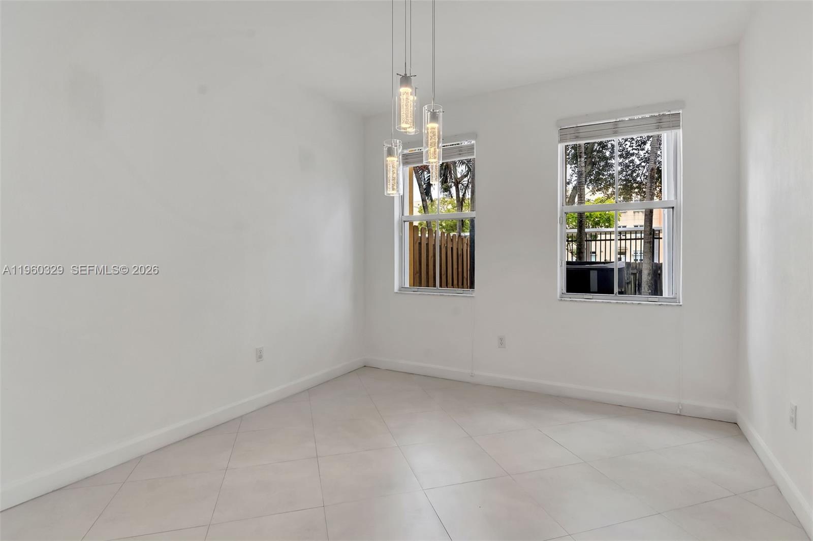 An empty room with white walls, light tile flooring, two windows, and a pendant light — 11321 NW 84th St, Doral FL 33178, DORAL, FL