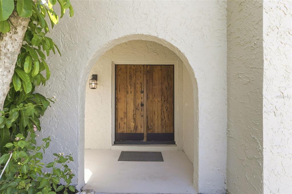 A rustic wooden double door sits within a white arched entryway of a stucco home — 4072 VANET COURT, ORLANDO, FL
