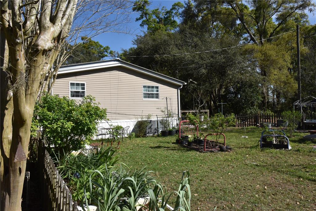 The exterior of a tan mobile home sits in a grassy backyard with garden beds — 6482 SE 55TH STREET, TRENTON, FL