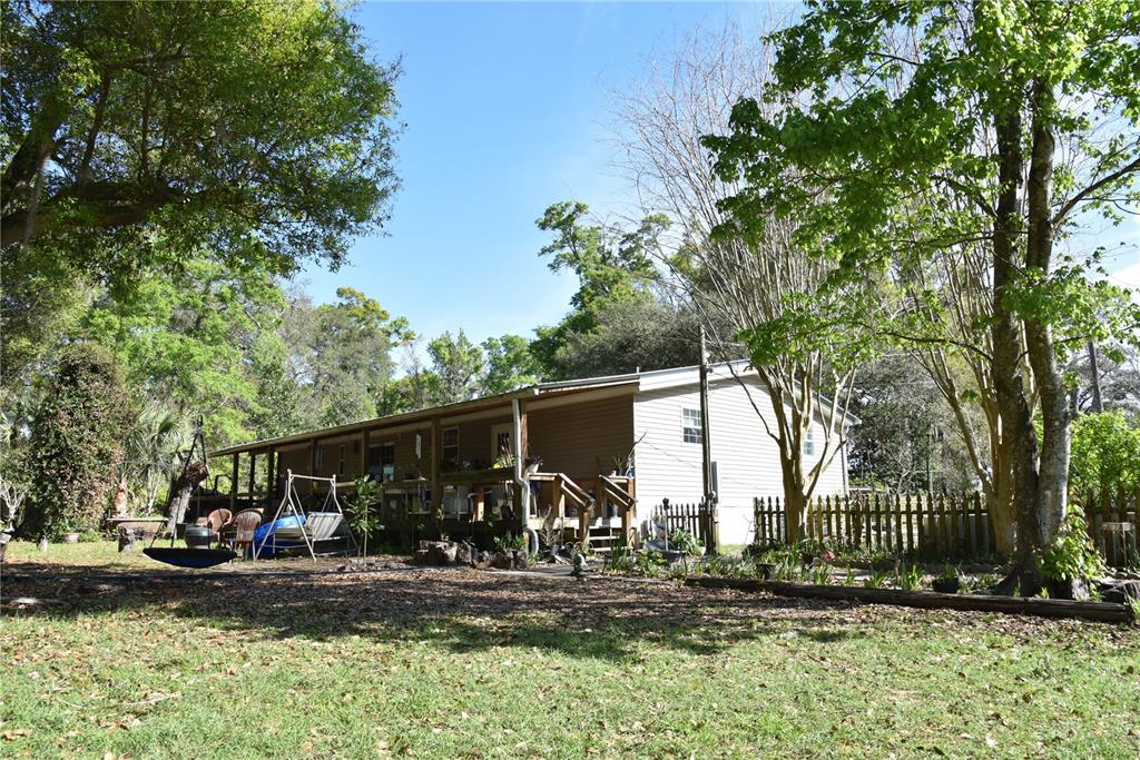 A single-story house with a wooden porch sits in a yard with many trees — 6482 SE 55TH STREET, TRENTON, FL