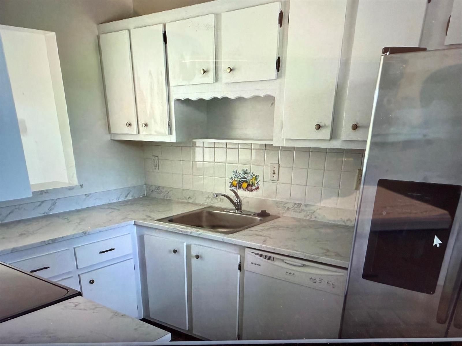 A kitchen features white cabinets, a stainless steel sink, marble-look countertops, and a white dishwasher — 5403 SE Miles Grant Road, Stuart FL 34997, STUART, FL