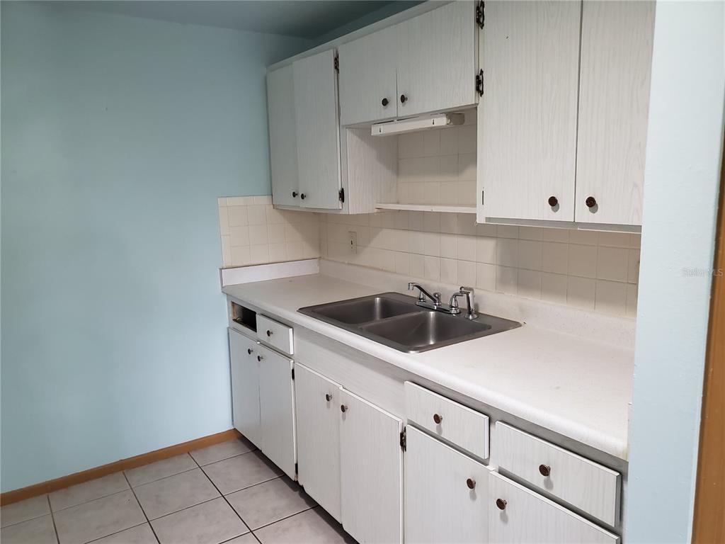 A kitchen features white cabinets, a double-basin stainless steel sink, and light-colored tiled flooring — 2021 PENNSYLVANIA AVENUE UNIT 5, ENGLEWOOD, FL