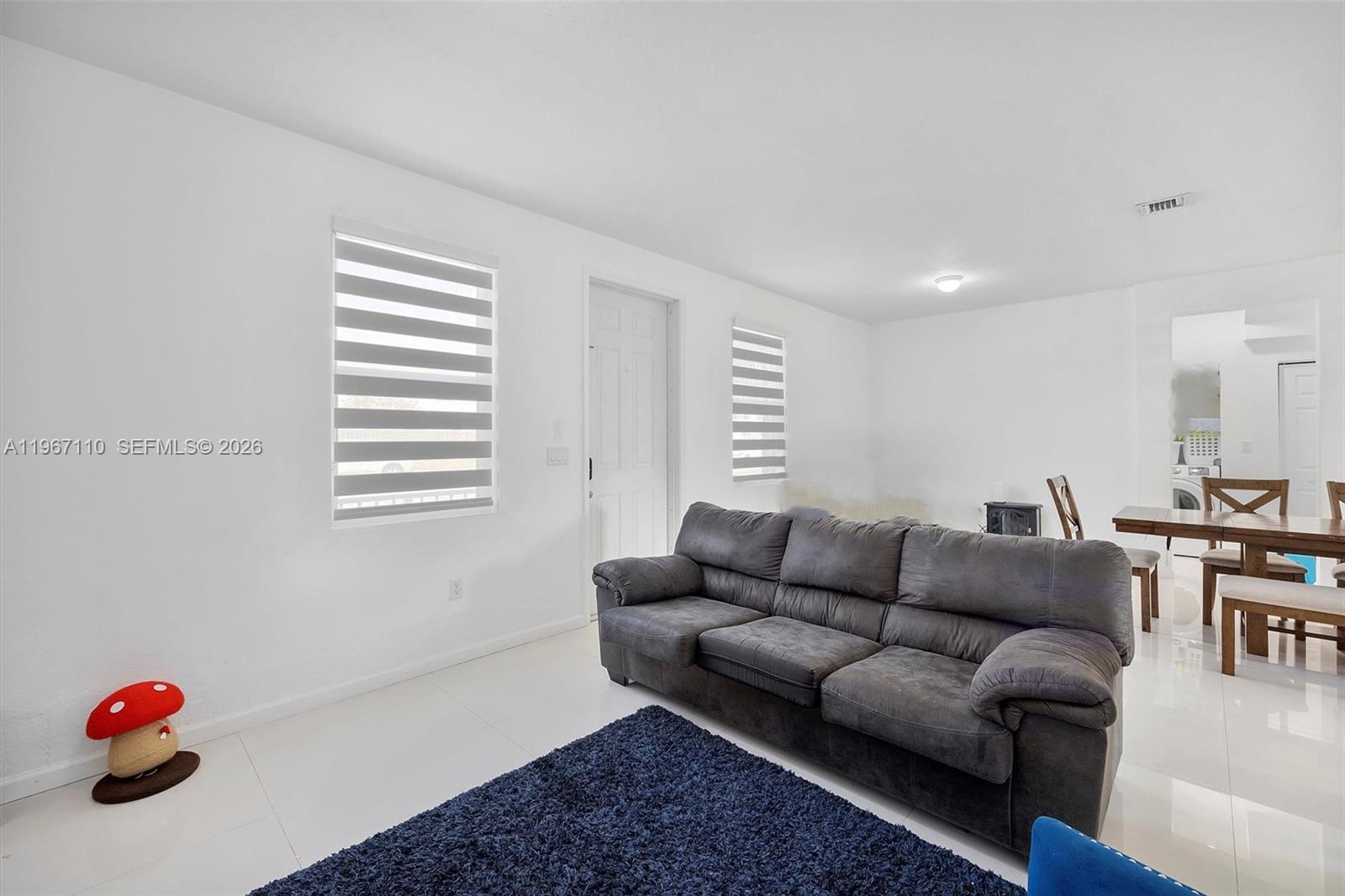 A living room features white walls, tile flooring, a dark sofa, and a blue rug — 24557 SW 117th Ave, Homestead FL 33032, HOMESTEAD, FL