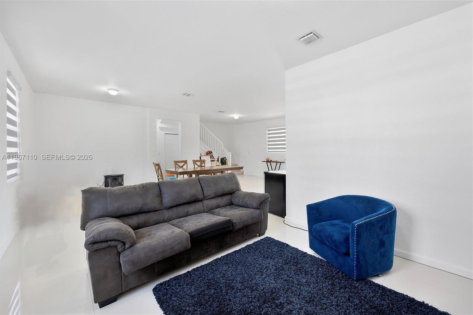 A living room features a grey sofa, a blue armchair, and a dining area — 24557 SW 117th Ave, Homestead FL 33032, HOMESTEAD, FL